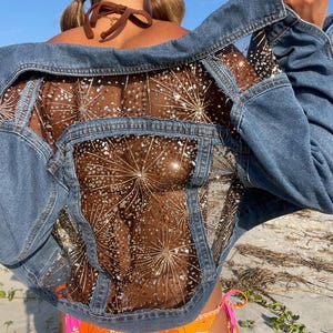 May include: A blue denim jacket with a sheer mesh back panel featuring a sparkly gold design. The jacket is open and the back panel is visible.