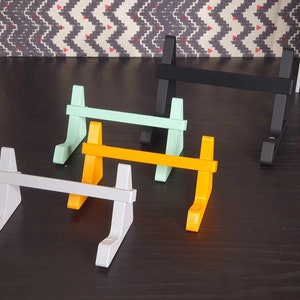 May include: Four different colored phone stands made of plastic. The stands are in various colors, including gray, yellow, green, and black.