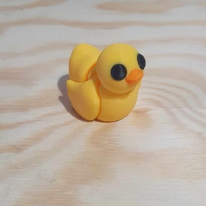Op de afbeelding: Een klein geel rubberen eendje met zwarte ogen en een oranje snavel.