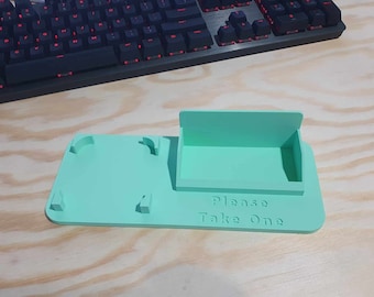 May include: A light green plastic phone stand with a slot for a phone and the words "Please Take One" printed on the bottom.