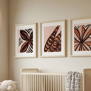 Op de afbeelding: Drie ingelijste abstracte kunstprints met een roze en bruine kleurstelling. De prints tonen gestileerde bloemmotieven.