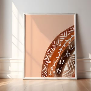 Könnte beinhalten: Ein gerahmter Kunstdruck mit einem stilisierten Regenbogen-Design. Das Kunstwerk zeigt eine warme Farbpalette mit Braun- und Weißtönen und einem pfirsichfarbenen Hintergrund. Das Regenbogen-Design hat geometrische und florale Muster.
