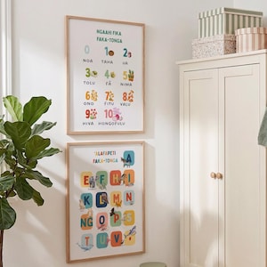 May include: Two framed educational posters hanging on a white wall. The top poster displays numbers zero through ten in Tongan with corresponding illustrations. The bottom poster features the Tongan alphabet with colorful letter blocks and animal icons.