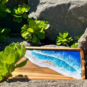 Pu&ograve; includere: Un vassoio da portata in legno con un design a onda oceanica in resina blu e bianca. Il vassoio &egrave; rettangolare e ha una finitura in legno naturale.