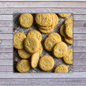 May include: A close-up of a wire rack filled with freshly baked, golden brown sugar cookies. The cookies are arranged in a random pattern, with some overlapping.