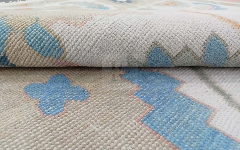 May include: Close-up of a beige and white rug with a geometric pattern in shades of blue and pink. The rug has a soft, textured surface.