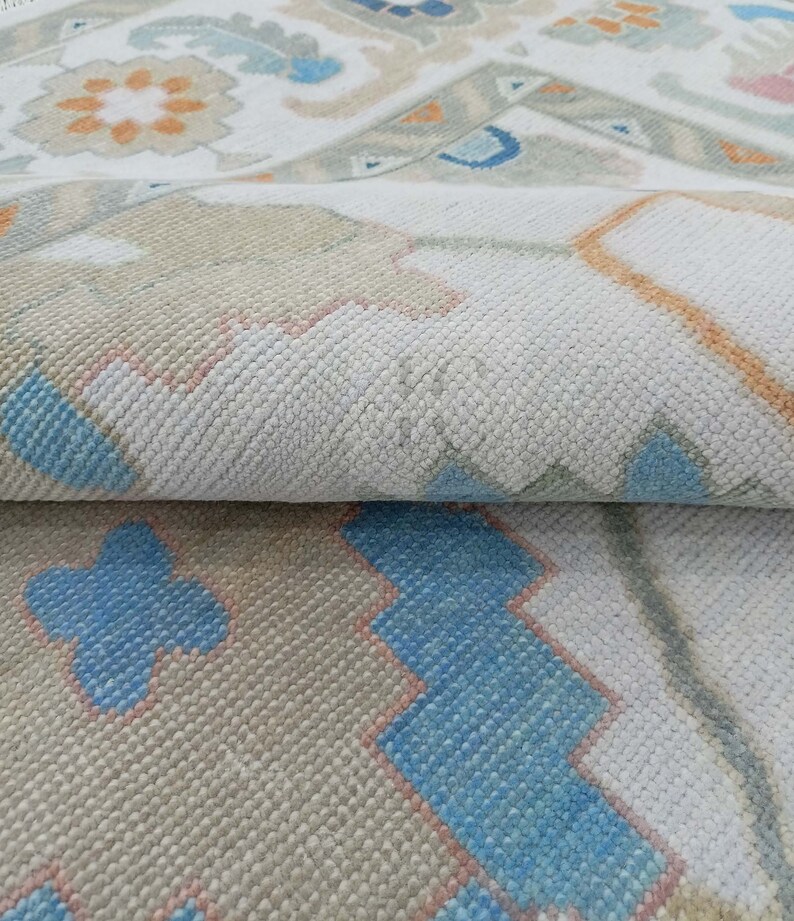 May include: Close-up of a white rug with a geometric pattern in shades of blue, orange, and pink. The rug has a soft, textured surface.