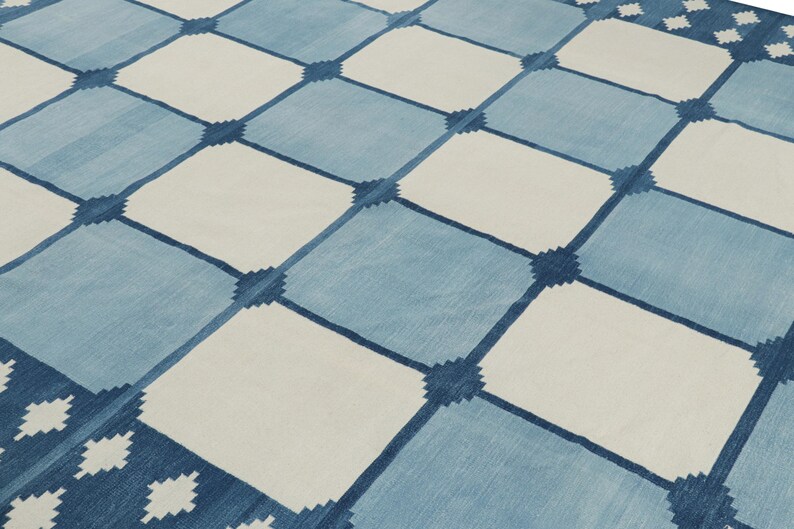 May include: A flat-woven rug featuring a repeating grid pattern of alternating light blue and off-white squares. The intersections of the grid are marked by small, dark blue geometric star-like motifs that connect the larger square sections.