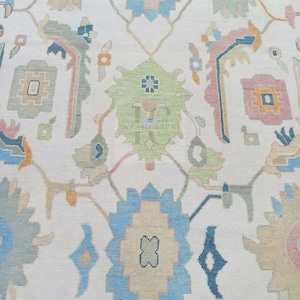 May include: A white rug with a repeating pattern of blue, green, and pink floral designs. The rug has a woven texture and a subtle sheen.