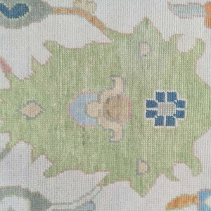 May include: A close-up of a cream-coloured rug with a green, blue, and orange floral pattern. The rug has a subtle texture and a traditional design.