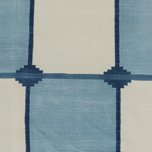 May include: A woven textile featuring a grid pattern of alternating light blue and off-white squares. The grid lines are defined by dark navy blue horizontal and vertical bands, with small, stepped, cross-shaped motifs at each intersection.