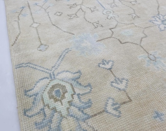 May include: A beige rug with a floral pattern in light blue and brown. The rug has a rectangular shape and a textured surface. The floral design is spread across the rug's surface.