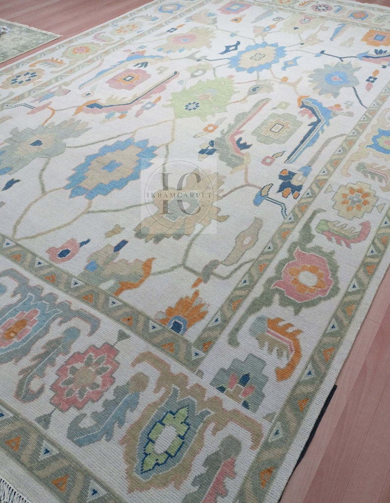 May include: A cream-coloured rug with a traditional Persian design. The rug features intricate patterns in shades of blue, green, pink, and orange. The rug has a fringed border.