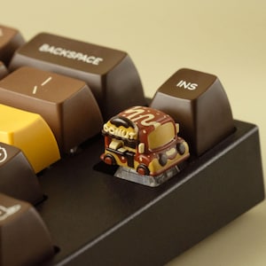 May include: A custom mechanical keyboard with brown and yellow keys. A novelty keycap shaped like a donut truck is installed. The keycaps have white text and dog illustrations. The Enter key is yellow.