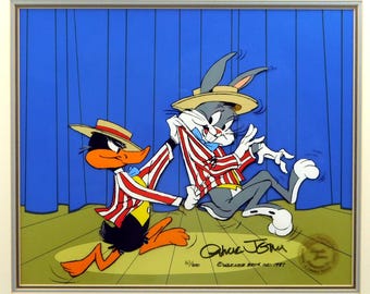 May include: A framed animation cel featuring Bugs Bunny and Daffy Duck in matching red and white striped jackets and straw hats. Daffy pulls at Bugs' jacket. The background is a blue curtain. Signed by Chuck Jones.