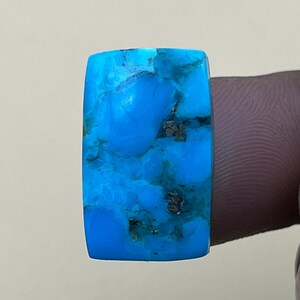 May include: A bright blue turquoise cabochon with a marbled pattern. The stone is rectangular and has a smooth, polished surface.