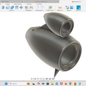 May include: A 3D model of a speaker with a gray, rounded, cylindrical shape. The speaker has two large circular openings, one on the front and one on the side. The speaker is designed to resemble a jet engine.