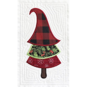 Può includere: Un cappello da gnomo rosso e nero a quadri si trova in cima a un albero di Natale verde e rosso con un tronco marrone. L'albero è circondato da uno sfondo trapuntato bianco.