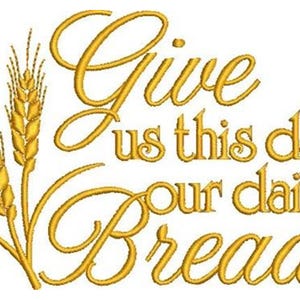 May include: Gold embroidered design on a white background. The text reads "Give us this day our daily bread" in elegant script. Two stalks of wheat are on the left side of the text. The design is suitable for embroidery projects.