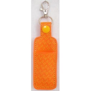 May include: Orange leather keychain with a small pocket and a yellow button. The keychain has a silver metal hook.