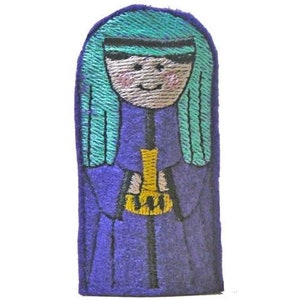 May include: Embroidered patch featuring a stylized figure with teal hair and a purple robe. The figure holds a gold object. The patch has a white background and is likely designed for clothing or accessories.