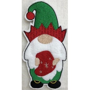 May include: Embroidered felt gnome ornament with a green hat, red and white patterned shirt, and black shoes. The gnome is holding a red and white patterned gift.
