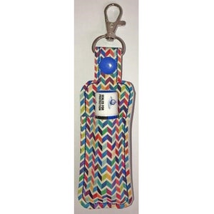 May include: A colorful chevron patterned fabric key chain with a snap closure and a silver key ring. The key chain has a pocket for a lip balm tube. The lip balm tube is white with blue text that reads "Sealed for Protection".