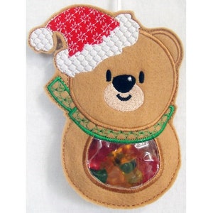 May include: A brown felt Christmas stocking shaped like a bear wearing a red and white Santa hat. The stocking has a clear plastic window showing colorful gummy candies inside.