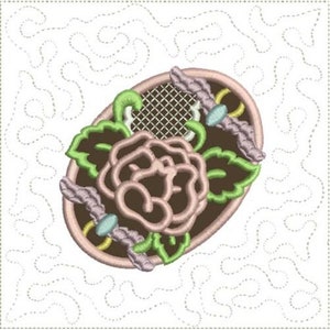 May include: A pink oval-shaped embroidery design with a brown rose and green leaves. The design is surrounded by a white background with a light brown, dotted, swirling pattern.