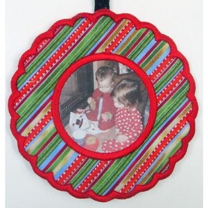 May include: Red and green striped fabric ornament with a scalloped edge and a red frame with a photo of two children inside.