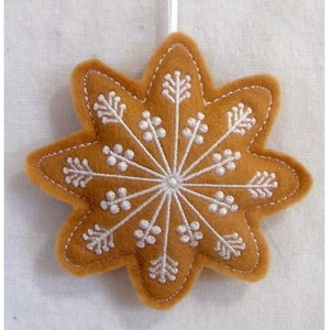 May include: A tan felt star-shaped ornament with a white embroidered snowflake design.