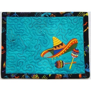 May include: A turquoise blue quilted coaster with a colorful embroidered sombrero and maracas. The coaster has a black border with a colorful pattern.