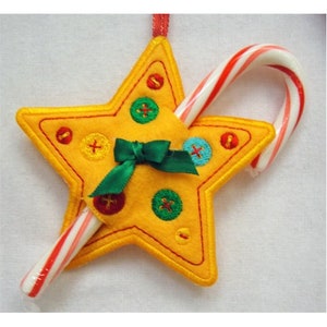 May include: A yellow felt star-shaped ornament with a red and white candy cane tucked inside. The star is decorated with colorful buttons and a green bow.