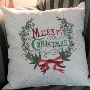 May include: White throw pillow with a red, green, and white floral wreath design. The wreath surrounds the text "Merry Christmas".