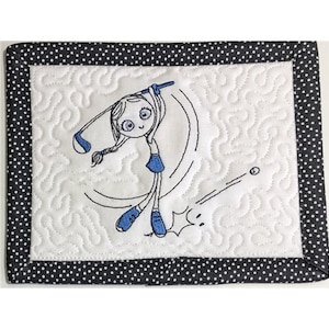 May include: A white quilted coaster with a black polka dot border. The coaster features an embroidered design of a girl playing golf.