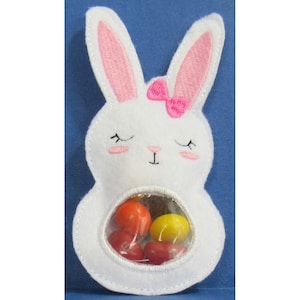 May include: White felt bunny with pink ears and a pink bow. The bunny has a clear plastic window on its belly, filled with colorful candy.