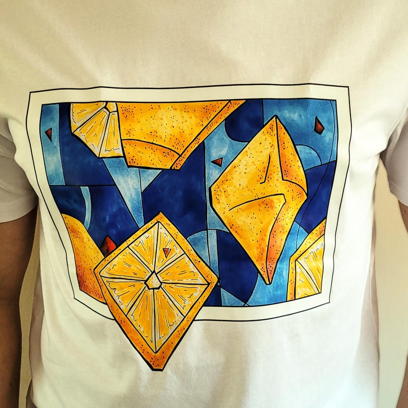 May include: White t-shirt featuring a vibrant, geometric design of yellow lemon slices and abstract shapes against a blue background. The artwork is framed with a black border, creating a modern and artistic look. The shirt is made of a soft, comfortable material.