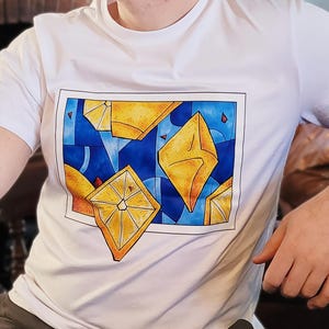 May include: White t-shirt featuring a vibrant graphic design. The design showcases yellow geometric shapes against a blue background, with red accents. The artwork is framed within a black border, creating a modern and eye-catching aesthetic.