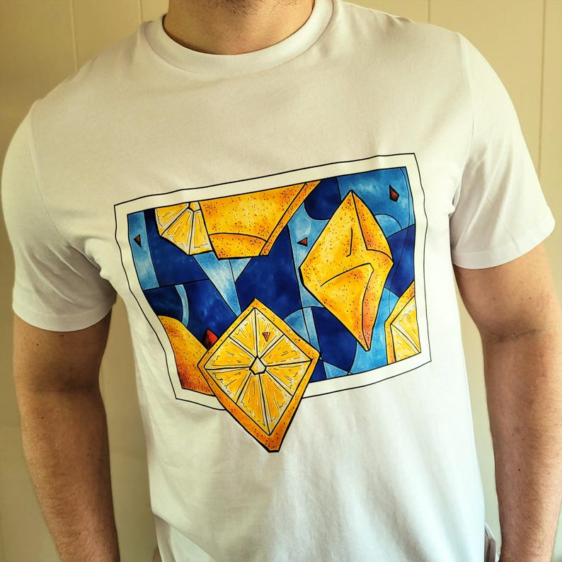 May include: White t-shirt featuring a geometric design of yellow and orange shapes against a blue background. The design is framed with a black border. The shirt is made of a soft, comfortable material.