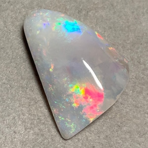 Op de afbeelding: Een witte opaal edelsteen in een traanvorm met iriserende flitsen van blauw, groen, roze en geel.