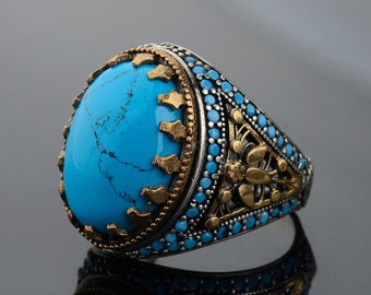 May include: A silver ring with a large turquoise stone set in a gold-toned filigree design. The ring is surrounded by smaller turquoise stones.