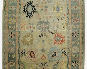 May include: A rectangular area rug with a central field of muted green, adorned with floral and geometric patterns in shades of blue, peach, and yellow. The rug features a border in a darker green with floral motifs.