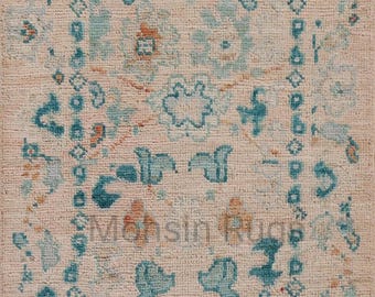 May include: A beige rug with a detailed pattern of teal and orange floral and geometric shapes. The rug has a fringe along the top edge and the text "Monsin Rugs" is visible.