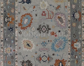 May include: A gray area rug with a floral pattern. The rug features a central field of gray with various floral motifs in shades of orange, blue, yellow, and purple. A darker gray border frames the design, adding contrast and definition to the rug's overall aesthetic.