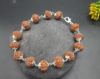 May include: A brown bracelet with silver beads and a silver clasp. The bracelet is made of rudraksha beads, which are believed to have spiritual and healing properties.