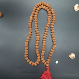 Può includere: Una collana di mala di legno marrone con un nappa rossa. Le perle sono rotonde e hanno una superficie testurizzata. La collana è infilata su un filo rosso.