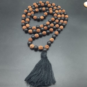 Può includere: Una collana di perline nere e marroni con un fiocco nero. Le perline sono in legno e sono infilate su un cordoncino nero.