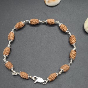 Peut inclure: Un bracelet marron et argent avec des perles de forme ovale. Les perles sont faites de matériaux naturels et sont enfilées sur une chaîne en argent.