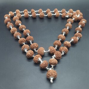 Può includere: Una collana mala marrone con perline d'argento e un nappina. La collana è realizzata con perline di rudraksha, che si ritiene abbiano proprietà spirituali e curative.