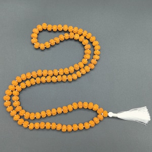 Può includere: Una collana di perle mala marrone con un fiocco bianco. La collana è fatta di perle rotonde ed è infilata su un cordoncino bianco.